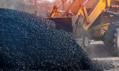 Hot asphalt delivered for roadworks. Roadworkers resurfacing the road during roadworks