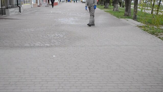 Man in protective suit spraying antiseptic solution on sidewalk in city. Persona disinfecting spray chemicals to preventing spread coronavirus. Sanitary measures in public place. Coronavirus pandemic