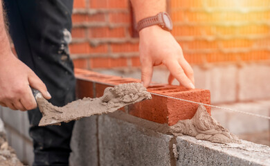Bricklayer laying brick on cement mix on construction site close-up. Reduce the housing crisis by...