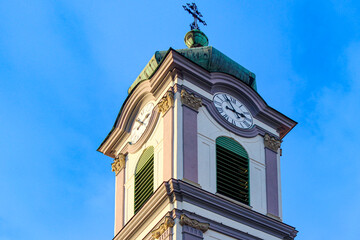 Purple and white baroque church tower with roof and cross covered with green patina, tower clock...