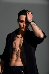Studio portrait of a young teenager brunette boy in a black shirt with a tattoo on his arm, a pendant and a bracelet. Elegant sexy style. Gray background.
