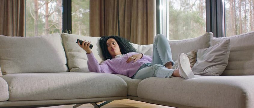 Black African-American female watching TV at home, sees something disgusting or scary