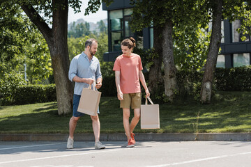 bearded father and teenage son walking with shopping bags outdoors.