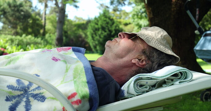 Man in 70s asleep outside. Older man with face covered with had napping siesta