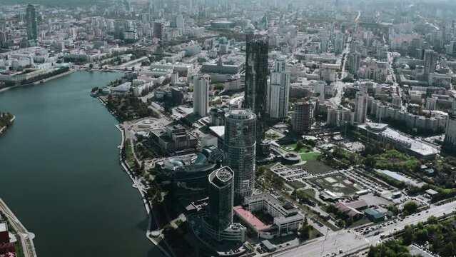 A built-up city under the bright sun. Stock footage. Huge glass offices and residential buildings standing next to the lake and walking areas.
