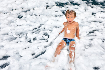 Enthusiastic joyful boy at the foam party, close-up of a kid among the foam, foam party for the little one