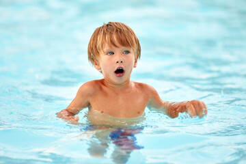 Fototapeta na wymiar Little boy in blue swimming trunks learns to swim in the pool, joy for children in the water park, children's swimming
