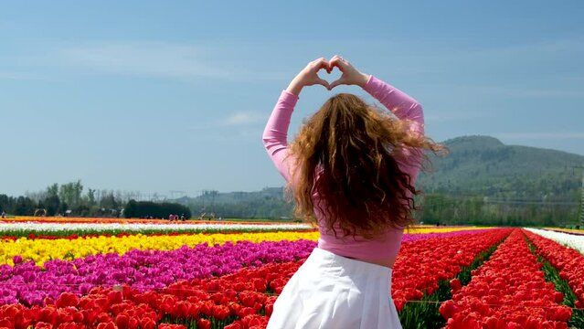 young woman making hands heart stands with back to camera in huge field of tulips spring festival joy dance movement jump jump rejoice unrecognizable people Tennis white skirt adolescence girl against