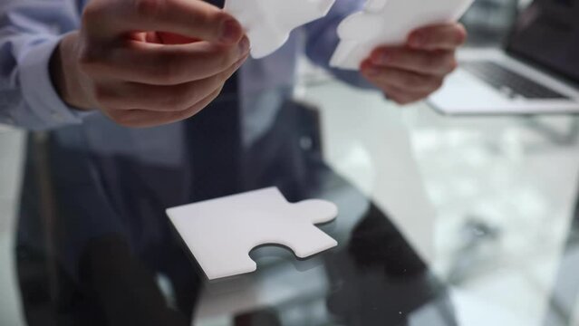 Man's hand in a suit holding one puzzle piece on a desk