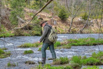 A hiker crosses a river in the wilderness. The river is not very deep, but it flows fast, with rocky sections. It moves cautiously because the rocks in the river bed are slippery... - Powered by Adobe
