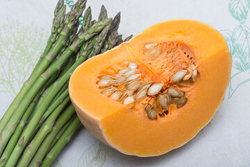 Piece of pumpkin and bunch of asparagus on a tablecloth. Vegetarian food. 