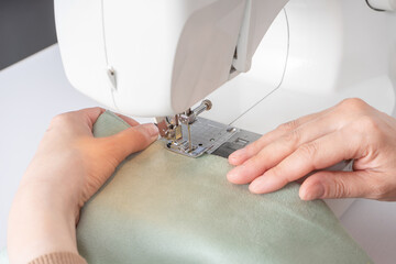 Female hands stitching white fabric on modern sewing machine at workplace in atelier. Women's hands sew pieces of fabric on a sewing machine closeup. Handmade, hobby, small business concept