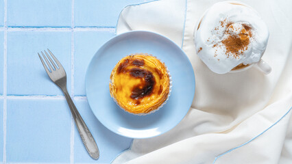Traditional Portuguese egg tart dessert Pasteis Pastel de nata or Pastels de Belem with a cup of capuchino coffee and fork on the blue tile. Flat lay