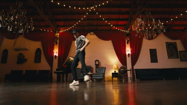 Dancing man in stylish hat performing floor spinning freestyle dance indoors in victorian style classic hall having fun. Vintage retro lifestyle happiness concept. Guy breakdancing street hiphop dance