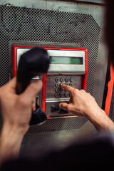 Person dialing a phone number on a public telephone at a payphone booth. Old school telecommunications technology. 