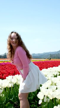 girl is spinning in field tulips wind raises skirt she bends down holding flowers in background laughter joy Youth fun cleanliness develop hair blue Clear sky modesty restraint cleanliness virginity