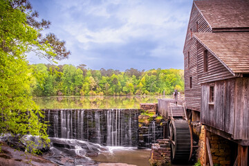 Landscape view of the millpond, waterfall, and gristmill at Historic Yates Mill County Park with...