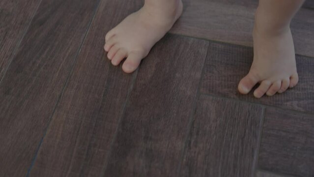 tiny barefoot legs baby child doing first steps, learning balancing stand still near window. Daytime sun beams light little toddler toes and heels. baby learn to walk stand on tip toes wooden floor. 