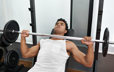 Bulking up his body. A young ethnic man lifting a heavy barbell.