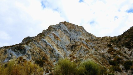 colorful mountain with clouds above and vegetation and bushes below
