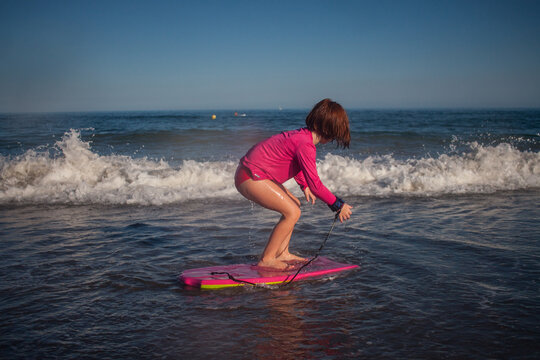ni&ntilde;a surfeando con camiseta rosa en la playa en verano con cielo azul