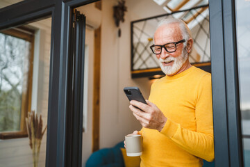 Senior Man Hold cup of coffee and Mobile Phone on Balcony happy smile