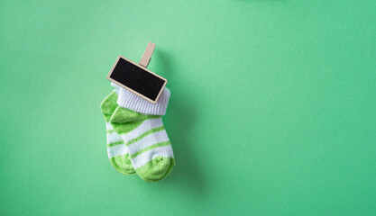 Green baby socks on a green background with a small board for writing with chalk. Versatile...