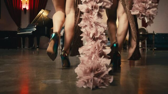 Female models walk runway in glamorous evening gown dresses with feathers. Hollywood style theatrical event with dance show performance in classy elegant interior. Legs and shoes only 4K RED camera