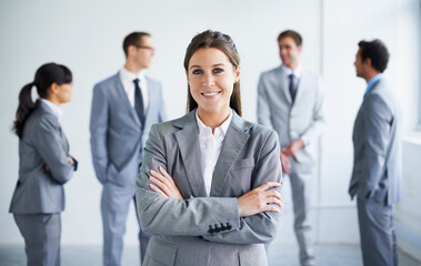 Confident in her business skills. A pretty young businesswoman smiling at you while her colleagues stand in the background.