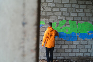 One young guy drawing graffiti on wall with spray can and mask on his face during the day