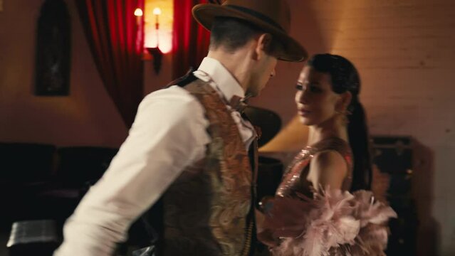 Passionate pair holding hands dancing in retro vintage night club atmosphere. Elegant guy holding woman spinning around. Glamorous lovers looking in the eyes while sensual woman performing sexy moves