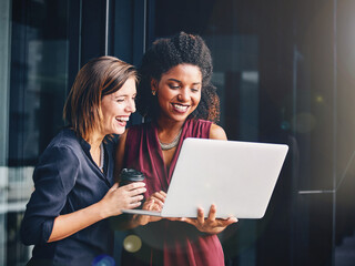 Working hard and having fun along the way. two young businesswomen using a laptop outside an office.