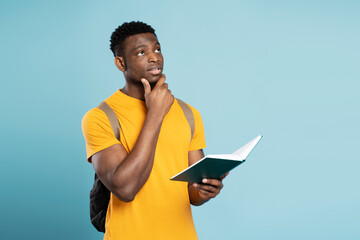 Portrait of pensive university student holding book studying, learning language, looking solution isolated on blue background. Education concept