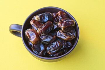  heap of dried fruit dates in a brown ceramic cup on a yellow table