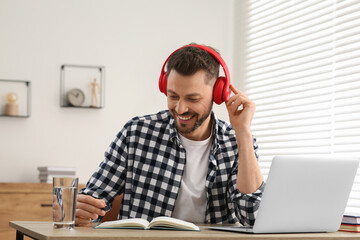 Naklejka premium Man in headphones studying on laptop at home. Online translation course