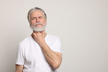 Senior man suffering from sore throat on white background, space for text. Cold symptoms