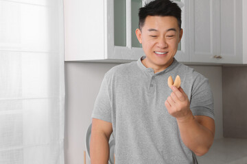 Happy asian man holding tasty fortune cookie with prediction indoors
