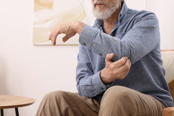 Senior man suffering from pain in his elbow at home, closeup. Arthritis symptoms