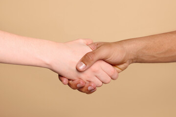 International relationships. People shaking hands on light brown background, closeup