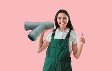 Happy female plumber with pipe showing thumb-up on pink background
