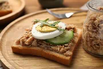 Delicious sandwich with tuna, greens, cucumber, boiled egg and spices on wooden board, closeup