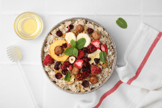Oatmeal with freeze dried fruits, nuts and mint on white tiled table, flat lay
