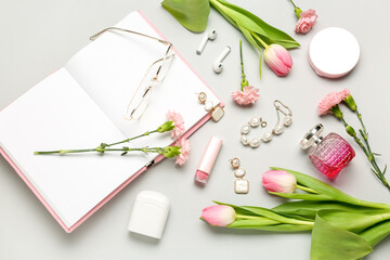 Composition with female accessories, cosmetics, earphones, notebook and spring flowers on light background