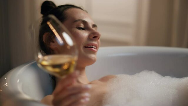 Carefree girl testing alcohol resting bathtub evening. Lazy woman enjoying spa