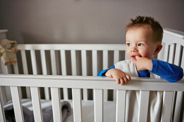 Sun is up and so am I. a cute little baby boy standing in his cot.