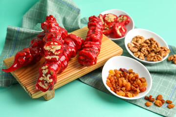 Wooden board with tasty churchkhela, pomegranate and walnuts on color background