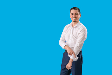 Young businessman rolling up his sleeve on light blue background