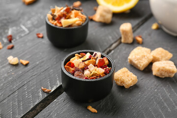 Bowls with dried fruit tea on black wooden table, closeup