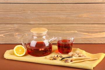 Teapot and glass of fruit tea on brown table near wooden wall