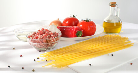 ingredients for spaghetti bolognese. pasta with minced meat and fresh vegetables on the table. tomatoes, paprika, onion, garlic and olive oil. illustration for a traditional dish recipe.